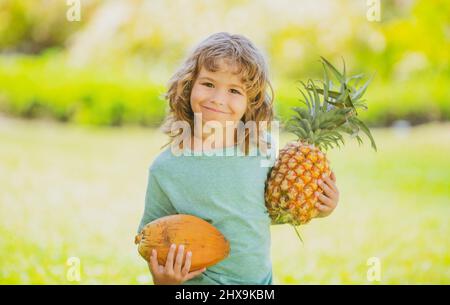 Child boy holding pineapple and coconut smiling with happy face. Summer fruits. Stock Photo