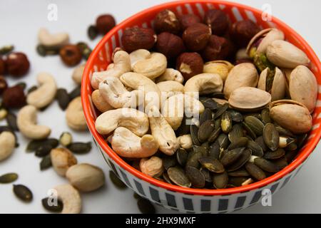 Close-up of a bowl with nuts in which there are walnuts, pumpkin seeds, hazelnuts and pistachios also scattered on the table Stock Photo