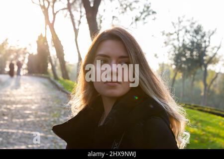 Young beautiful girl admires autumn nature landscape in lonely trip. Vivid morning in colorful forest with sun light. Happiness and finding peace. Stock Photo