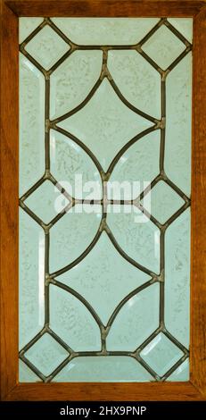 Glazed or frosted leaded glass window in wood frame with solder joints visible. The geometric pattern is repeating diamond shapes. Stock Photo