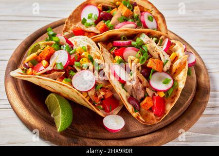 close-up of pitacos, mexican tacos with pita bread, spicy pulled chicken meat, red kidney beans, corn, radish, red pepper, roast sweet potatoes and li Stock Photo