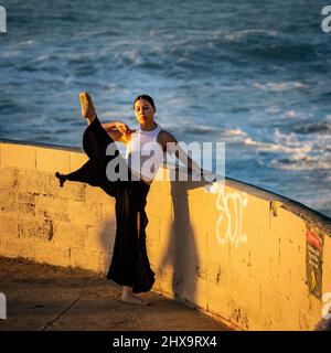 Young Multiracial Female Dancer on Wall Overlooking Crashing Waves Below Stock Photo