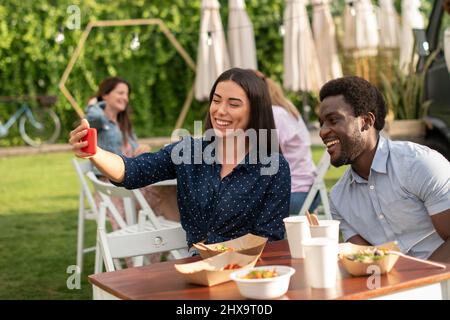 Positive multiethnic friends taking selfie in street cafe Stock Photo