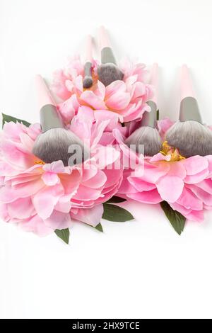 Different makeup brushes with pink peonies flowers on white background. Professional cosmetic makeup set. Accessories for beauty. Stock Photo