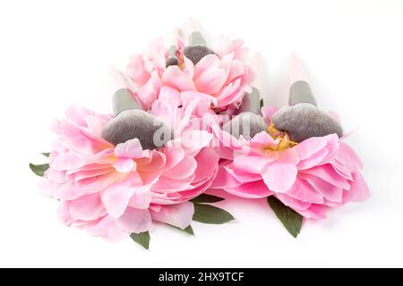 Different makeup brushes with pink peonies flowers on white background. Professional cosmetic makeup set. Accessories for beauty. Stock Photo