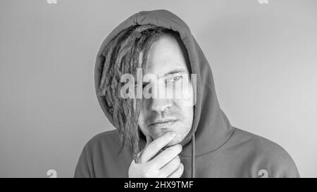Young man with red dreadlocks in hood with thoughtful look. Stylish male scratching chin and looking away. Black and white Stock Photo