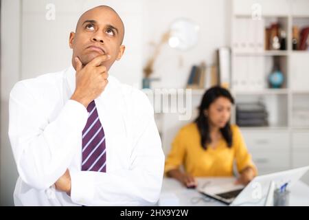 Portrait of pensive hispanic businessman standing in office Stock Photo