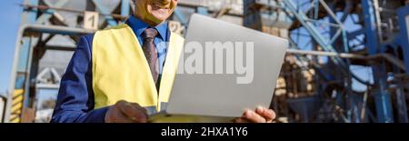 Cheerful male engineer using laptop outdoors at factory Stock Photo