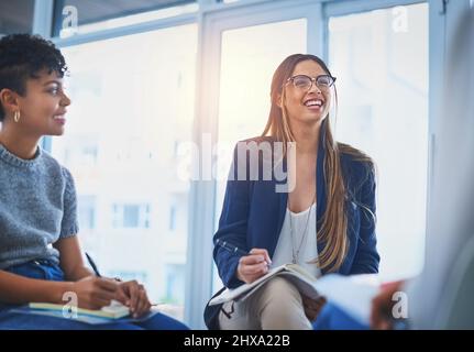 Taking notes at the office. Shot of two attractive young businesswomen taking down notes on their notepads during a meeting at work. Stock Photo