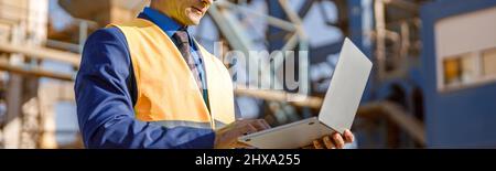 Male engineer working on laptop outdoors at factory Stock Photo