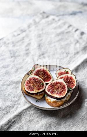 Two sandwiches with figs, cheese, thyme and honey on plate on gray linen napkin Stock Photo