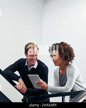 Discussing their plan for the day. Shot of two colleagues using a digital tablet while standing in a stairwell. Stock Photo