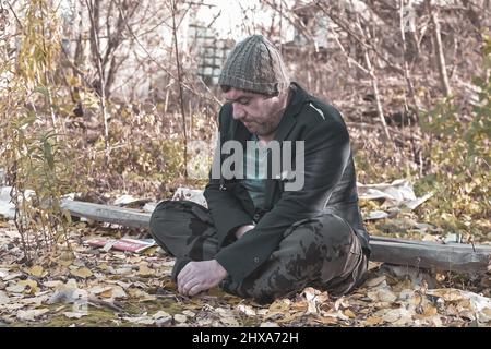 a poor homeless man with dirty hands smokes a cigarette in modern society. Economic recession, unemployment, poverty, hunger, pension, global crisis, Stock Photo