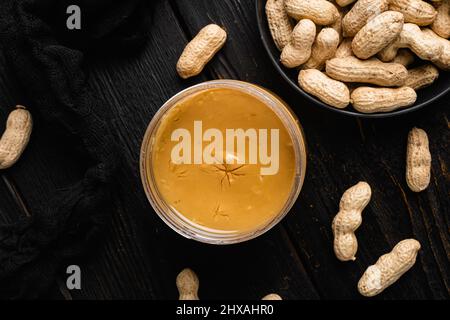 Peanut paste in an open jar and peanuts set, on black wooden table background, top view flat lay, with copy space for text Stock Photo