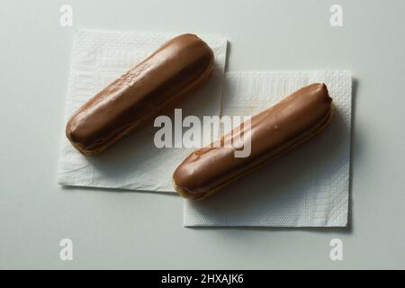 Two eclair with chocolate topping on the white napkins onn the white background Stock Photo