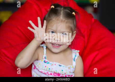 Portrait of cute child showing five sitting on the red armchair pear Stock Photo