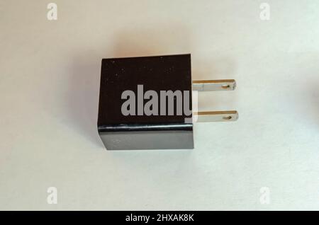 A black wall adopter charger with the two prang wal male plugs turning to the side is resting on a white surface. Stock Photo