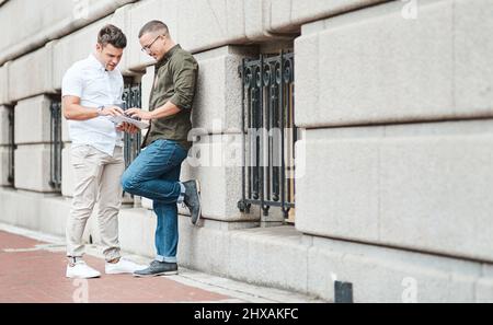 Two of the best in urban business. Shot of two young businessmen using a digital tablet together against an urban background. Stock Photo