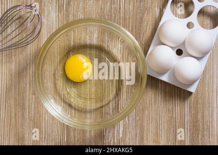 One raw chicken yolk and whites in glass bowl on the wooden table Stock Photo