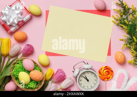 Easter composition. Eggs in the nest gift flowers rabbit ears alarm clock on a pink background. Empty sheet of paper with space for text Stock Photo