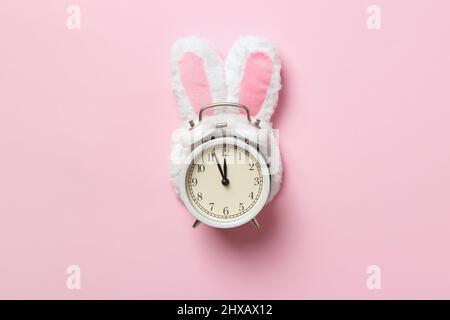 Easter time. Alarm clock in rabbit ears on a pink background. Stock Photo
