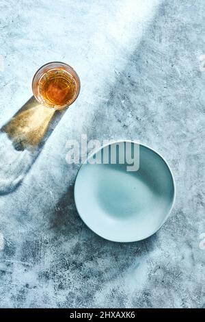 Top down shot of empty ceramic bowl and glass with drink casting shadows on textured rustic concrete background. Stock Photo