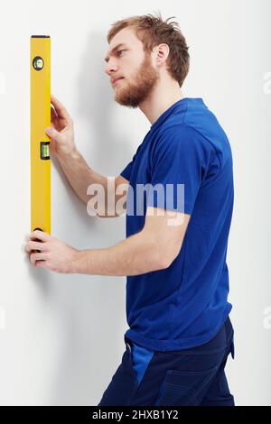 Making sure the wall is level. An unshaven young man using a level to make sure the wall is straight. Stock Photo