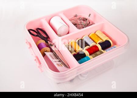 There are threads scissors and needles in a pink plastic sewing box. Isolated on white background Stock Photo