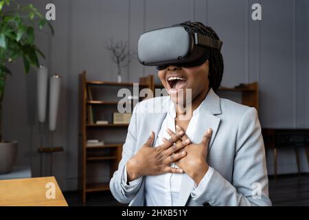 Emotional shocked african businesswoman in VR headset immersed in 3D virtual world screaming wow Stock Photo