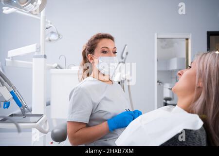 A female dentist in a dental office is talking to a patient and getting ready for treatment. copy space. Stock Photo