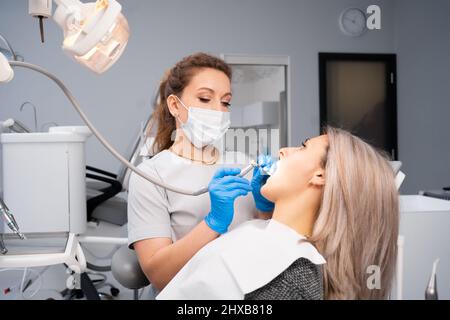 Dentist and patient in the medical center. The doctor treats the teeth of a young woman with a dental drill. Reception of an orthodontist and a prosth Stock Photo