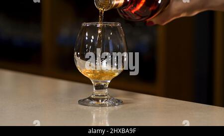 Close up of woman hand pouring cognac to the glass standing on the bar counter. Stock footage. Hand pouring alcohol into a glass on the blurred Stock Photo
