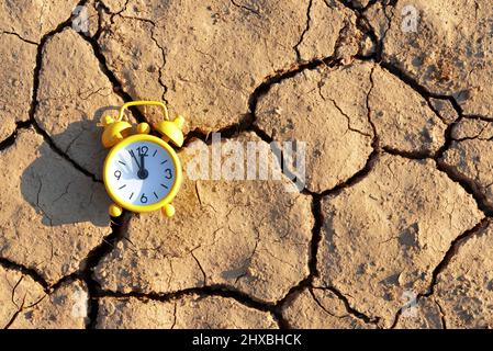 Alarm clock with five minutes before twelve o'clock on arid cracked soil. Concept of climate change or global warming. Stock Photo