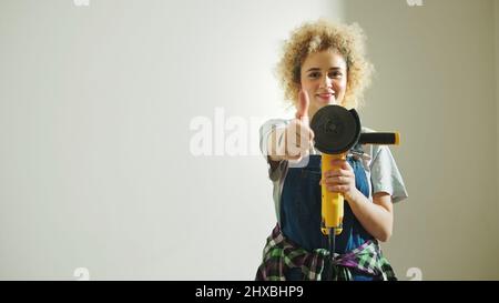 Attractive woman showing thumb up gesture while holding the angle grinder. High quality photo Stock Photo