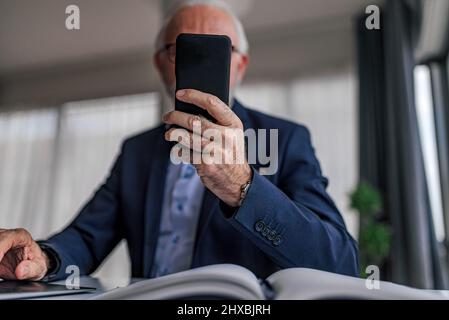 Faceless senior businessman entrepreneur holding smart phone directly in front of camera view. Unrecognizable mature business leader ceo manager using Stock Photo