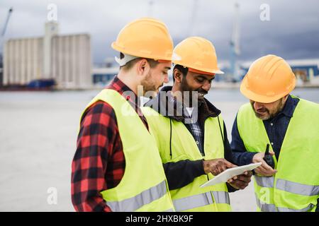 Workers controlling shipping containers at industrial port outdoor using tablet - Logistic business concept - Focus on indian man face Stock Photo