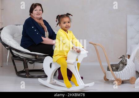 Grandmother and granddaughter from different races. The fair-skinned grandmother plays with the dark-skinned granddaughter. Stock Photo
