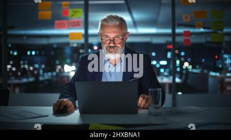 Successful Senior Businessman Working on Laptop Computer in Big City Office Late in the Evening. Investment Analyst Checking Financial Management Repo Stock Photo