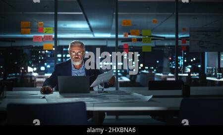 Successful Senior Businessman Working on Laptop Computer in Big City Office Late in the Evening. Investment Analyst Checking Financial Management Repo Stock Photo