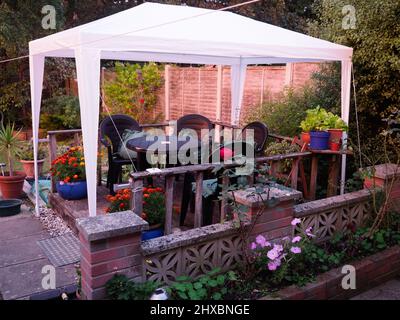 Plastic garden chairs and table under a white plastic gazebo on a small piece of wooden decking Stock Photo