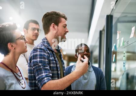 Hes making sure his plans are heard. Shot of a group of designers brainstorming with notes on a glass wall in an office. Stock Photo