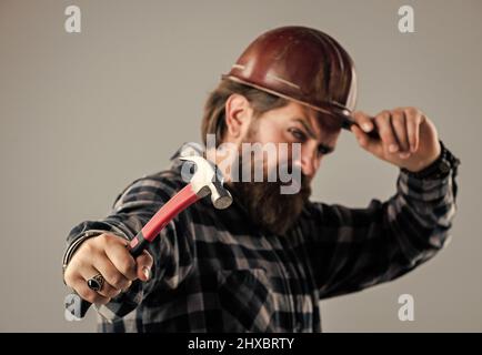 bearded male hipster in checkered shirt and laborer helmet, selective focus, hammer Stock Photo