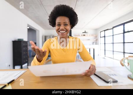 Smiling african american mid adult female freelancer with chart gesturing while sitting at home Stock Photo