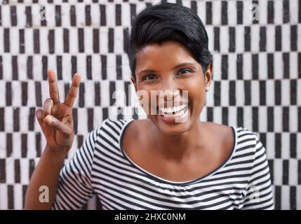 Black and white and bold. A cropped portrait of a beautiful young woman in stripes standing against a checkered wall. Stock Photo
