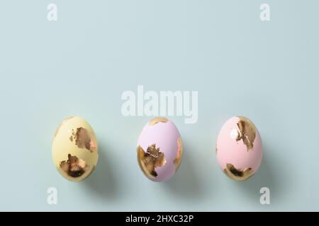 Three golden pastel eggs on blue background. Flat lay. Happy Easter greeting card with copy space. Top view. Stock Photo