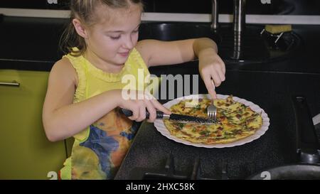 Smart girl learning to cook. Happy and serious young mistress children to cook a Neapolitan egg fried omelette from sausage. Modern Built In Kitchen A Stock Photo