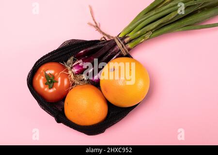 Close-up of oranges with tomato and scallion in black net on pink background Stock Photo