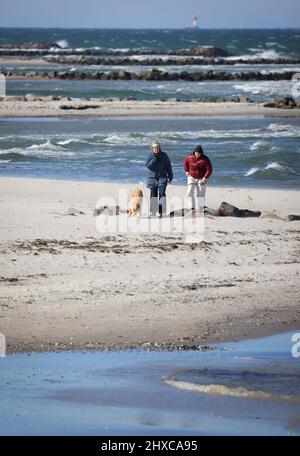 11 March 2022, Schleswig-Holstein, Schöneberg: People are walking on Schöneberg beach on the Baltic Sea in bright sunshine and strong wind. Photo: Christian Charisius/dpa Stock Photo