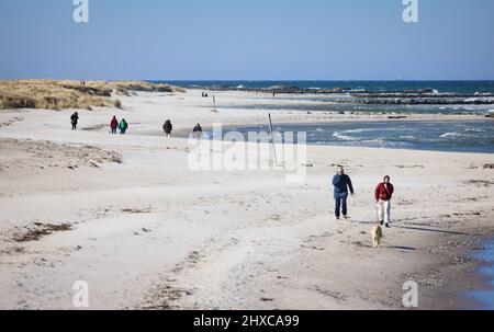 11 March 2022, Schleswig-Holstein, Schöneberg: People are walking on Schöneberg beach on the Baltic Sea in bright sunshine and strong wind. Photo: Christian Charisius/dpa Stock Photo