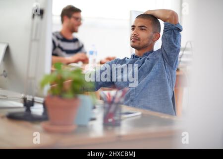 Trouble shooting modern problems. Serious young multi-ethnic man working at his desk in an open plan work space. Stock Photo